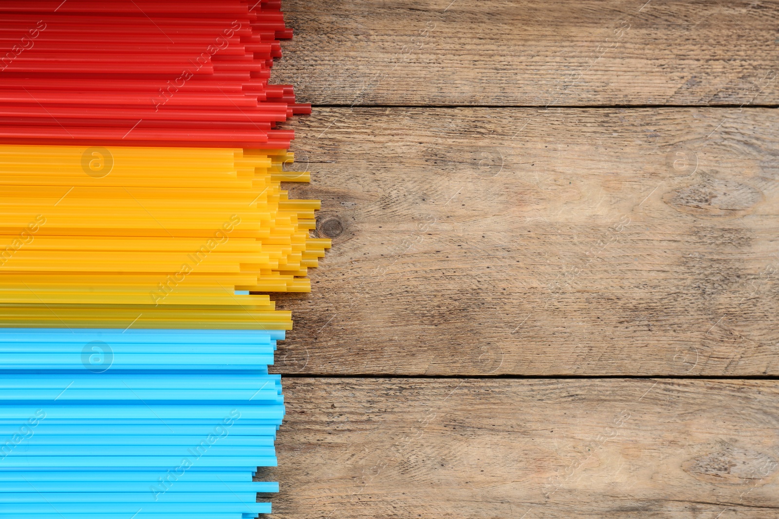 Photo of Colorful plastic drinking straws on wooden table, flat lay. Space for text