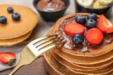 Photo of Tasty pancakes with chocolate paste, berries and fork on wooden table, closeup