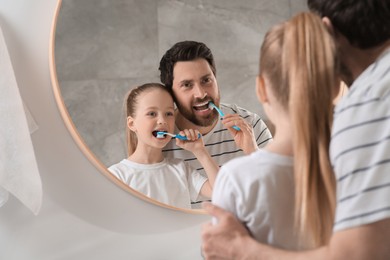 Photo of Father and his daughter brushing teeth together near mirror in bathroom