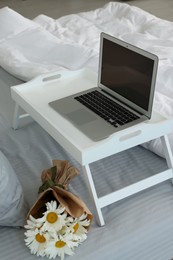 Photo of White tray table with laptop and bouquet of beautiful daisies on bed