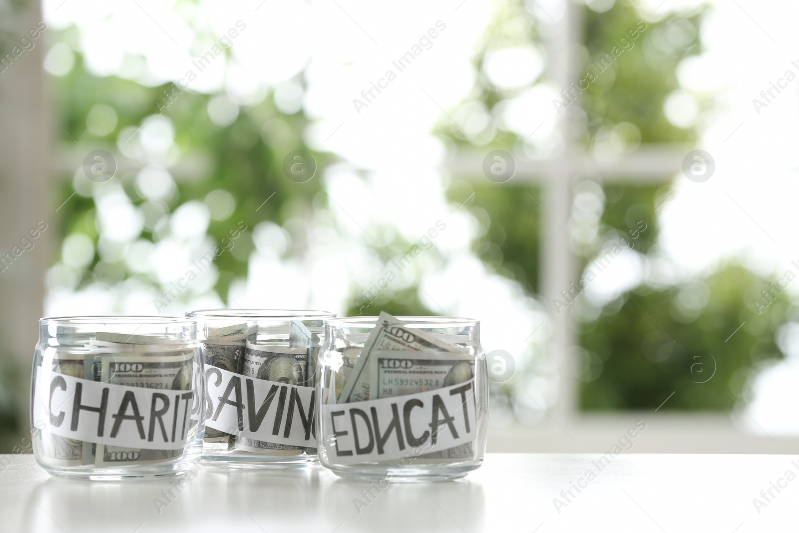 Photo of Glass jars with money for different needs on table against blurred background, space for text