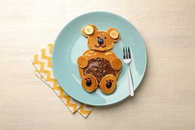 Creative serving for kids. Plate with cute bear made of pancakes, blueberries, bananas and chocolate paste on light wooden table, top view