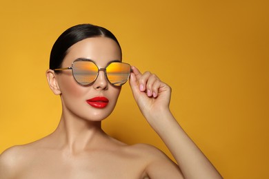 Image of Attractive woman in stylish sunglasses on orange background. Sea sunset reflecting in lenses. Space for text