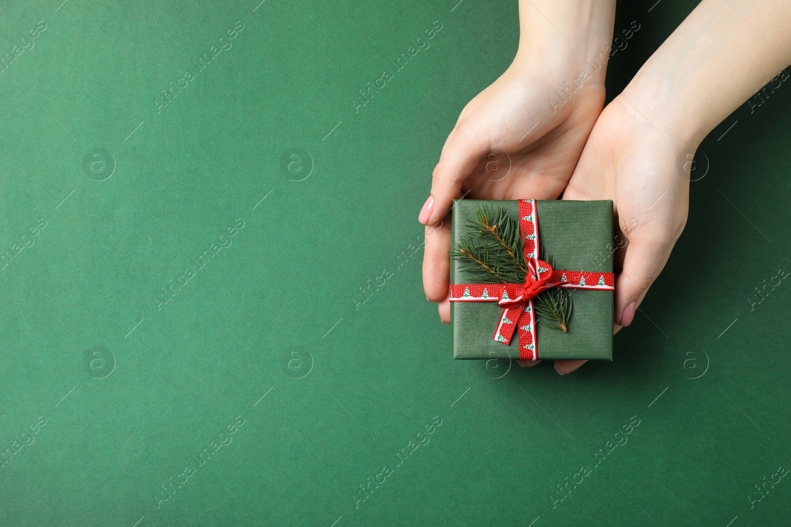 Photo of Woman holding beautifully wrapped Christmas gift box on dark green background, top view. Space for text