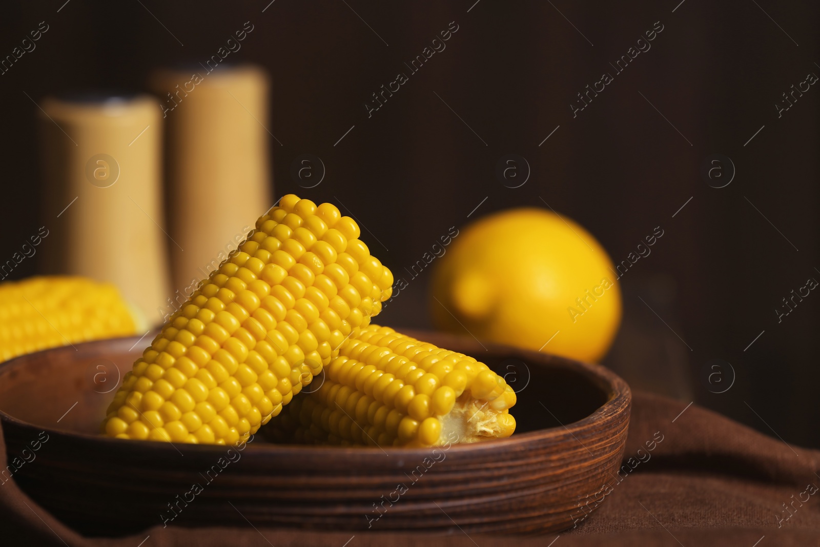 Photo of Plate with ripe corn cobs on table against dark background