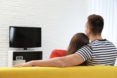 Photo of Couple watching TV together on sofa in living room. Space for text