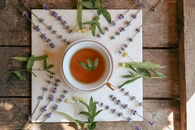 Photo of Tasty herbal tea and flowers on wooden table, flat lay