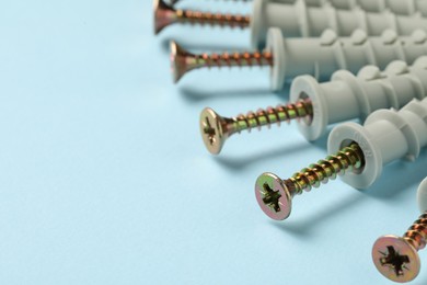 Many metal screws with dowels on light blue background, closeup. Space for text