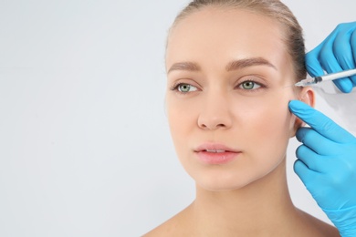 Photo of Young woman getting facial injection on white background. Cosmetic surgery concept