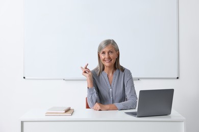 Photo of Happy professor giving lecture near laptop at desk in classroom, space for text