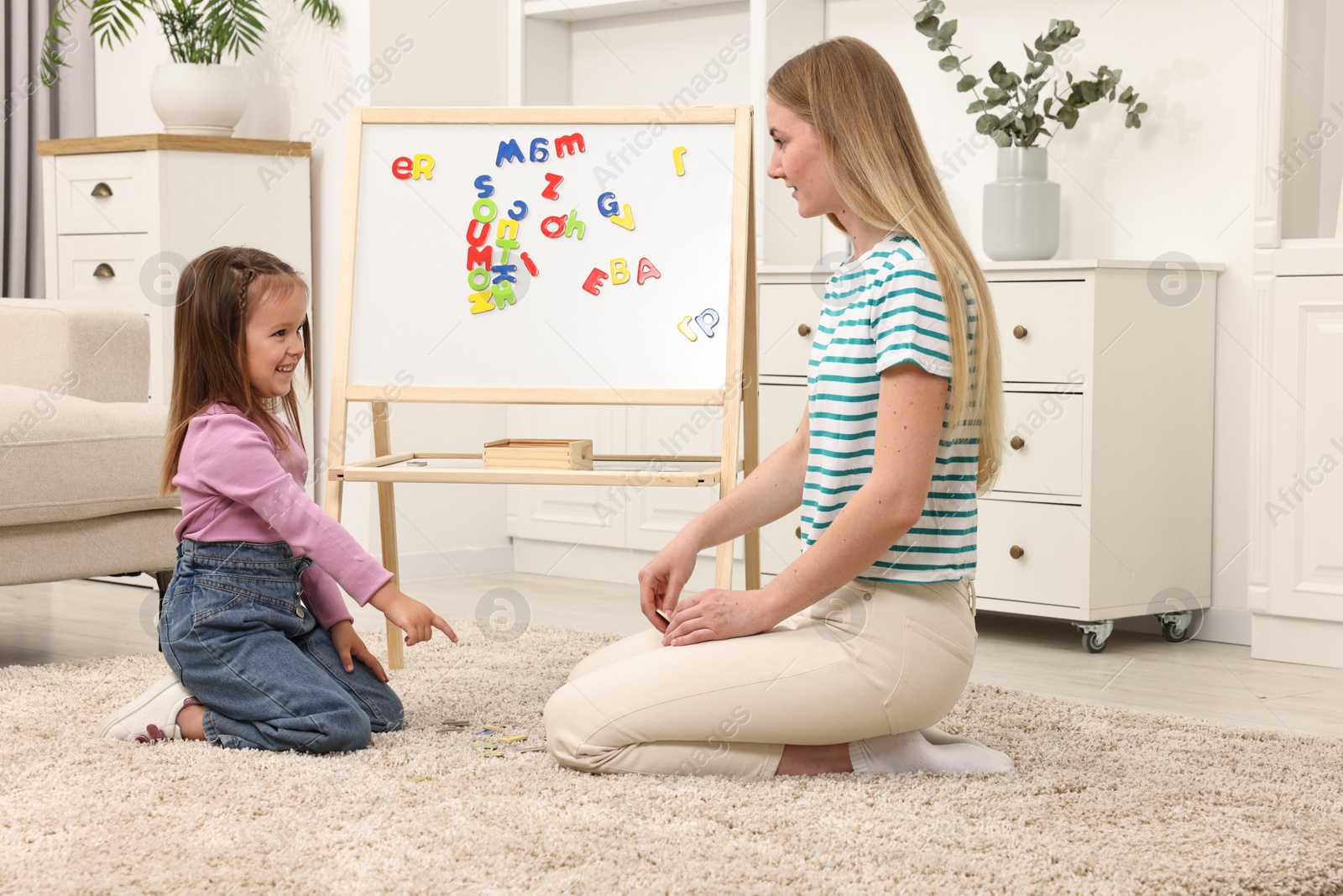 Photo of Mom teaching her daughter alphabet with magnetic letters at home