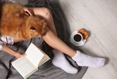 Woman with cute red cat and book on floor, top view. Space for text