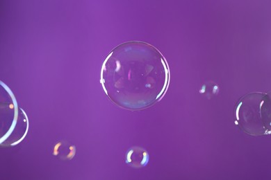 Beautiful transparent soap bubbles on violet background