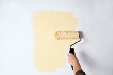 Photo of Woman painting white wall with beige dye, closeup