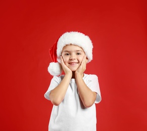 Cute little child wearing Santa hat on red background. Christmas holiday