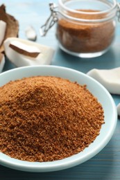 Photo of Natural coconut sugar in ceramic bowl on blue wooden table, closeup