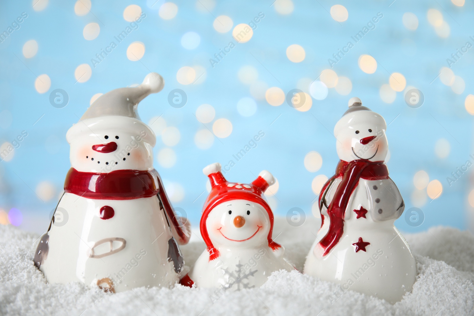 Photo of Decorative snowmen on artificial snow against blurred festive lights