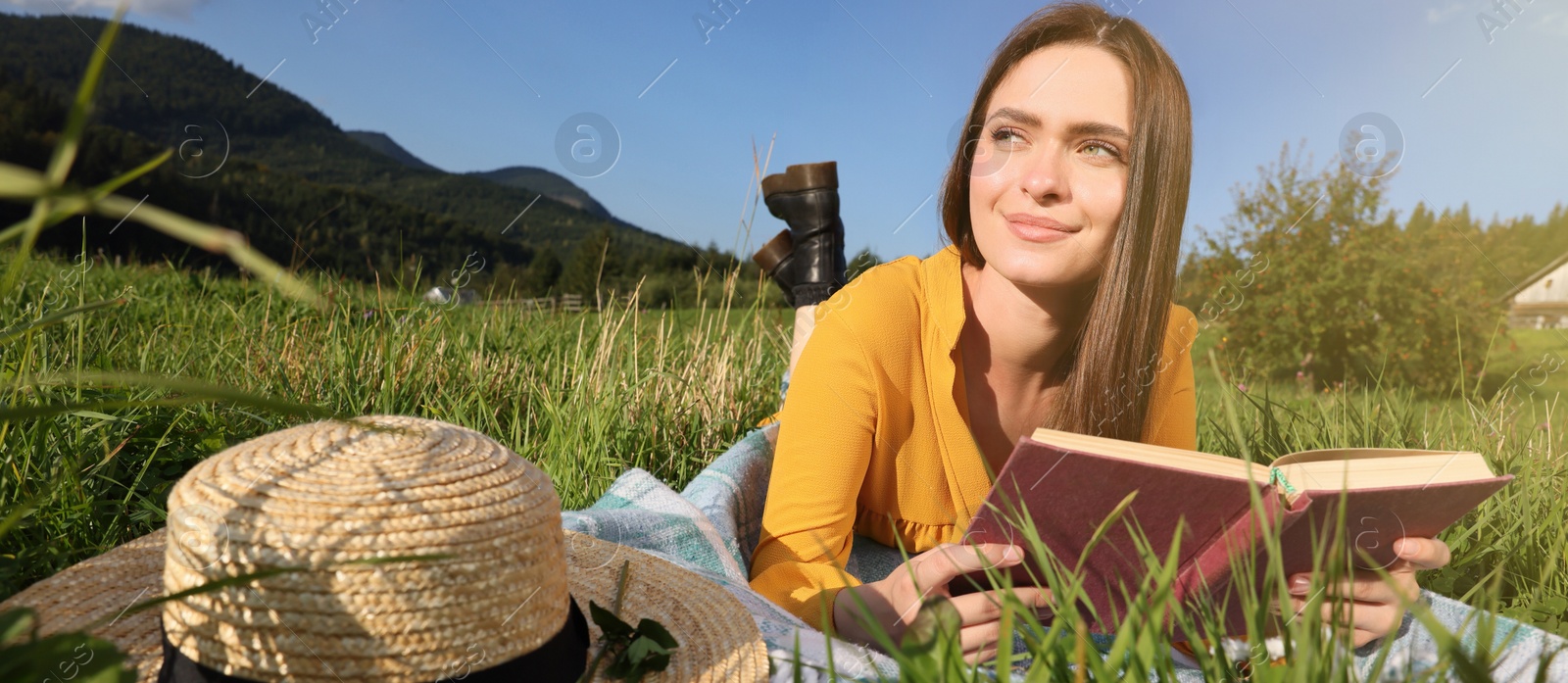 Image of Beautiful young woman reading book on green meadow in mountains. Banner design