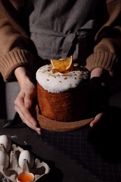 Young woman holding traditional decorated Easter cake over table, closeup