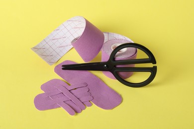 Photo of Scissors, bright kinesio tape roll and pieces on yellow background