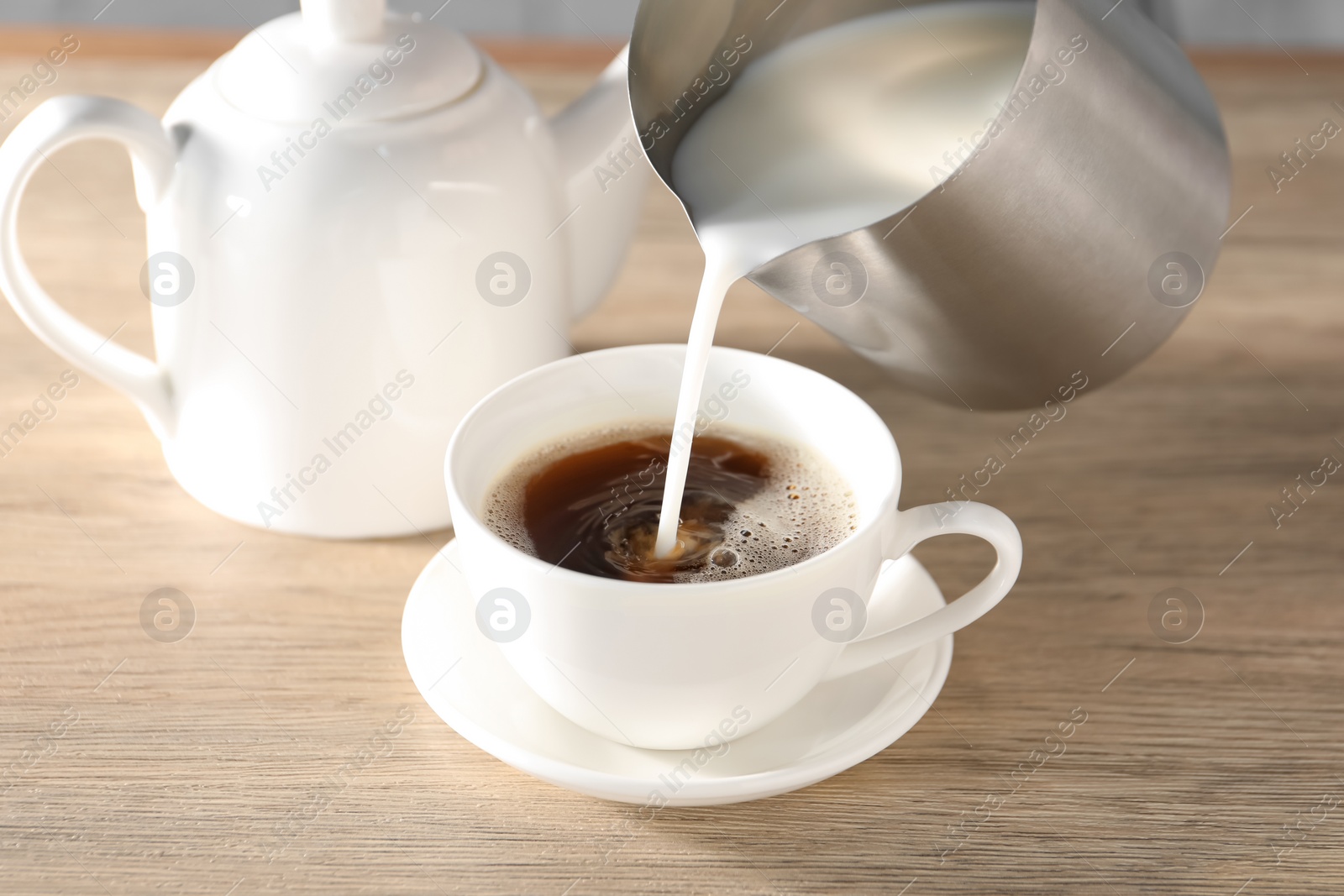 Photo of Pouring milk in tea at wooden table, closeup