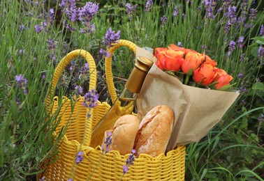 Yellow wicker bag with beautiful roses, bottle of wine and baguettes in lavender field