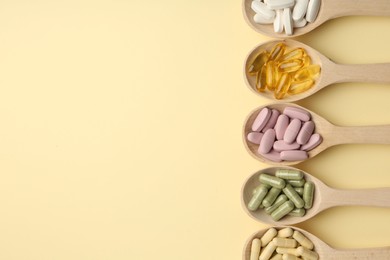 Photo of Different vitamin pills in spoons on pale yellow background, flat lay. Space for text