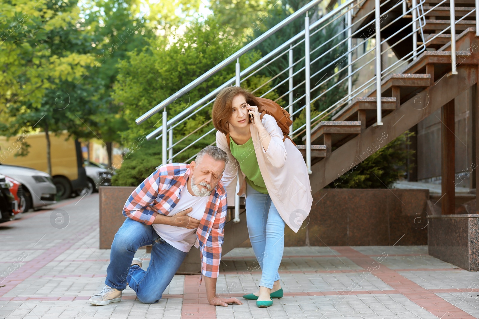 Photo of Woman calling ambulance for mature man having heart attack, outdoors