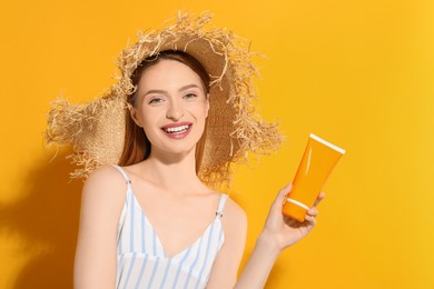 Photo of Beautiful young woman in straw hat holding sun protection cream on orange background, space for text