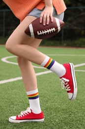 Photo of Woman with football ball wearing red classic old school sneakers on green court outdoors, closeup