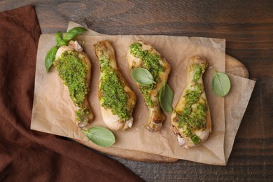 Delicious fried chicken drumsticks with pesto sauce and basil on wooden table, top view