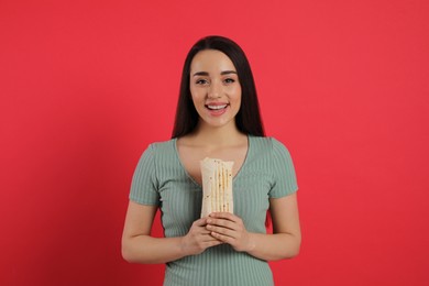 Photo of Happy young woman holding tasty shawarma on red background