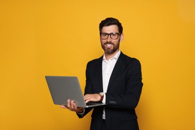 Photo of Portrait of smiling bearded man with glasses and laptop on orange background