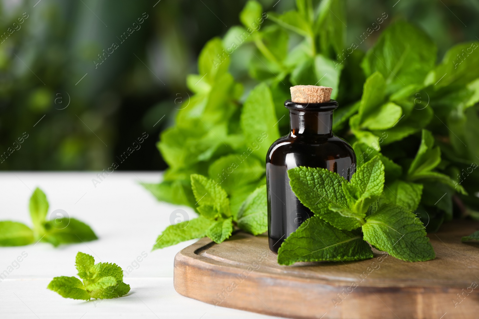 Photo of Bottle of mint essential oil and green leaves on white wooden table, closeup. Space for text