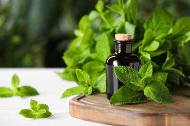 Photo of Bottle of mint essential oil and green leaves on white wooden table, closeup. Space for text