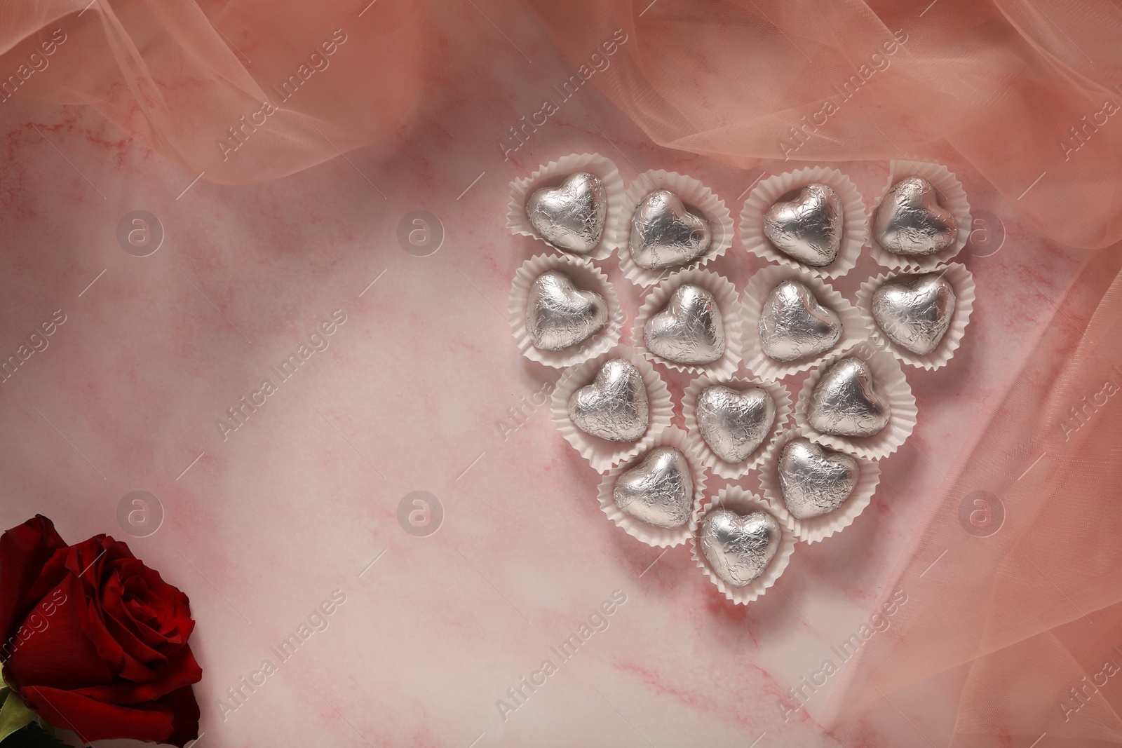 Photo of Heart made with delicious chocolate candies and beautiful rose on pink table, flat lay