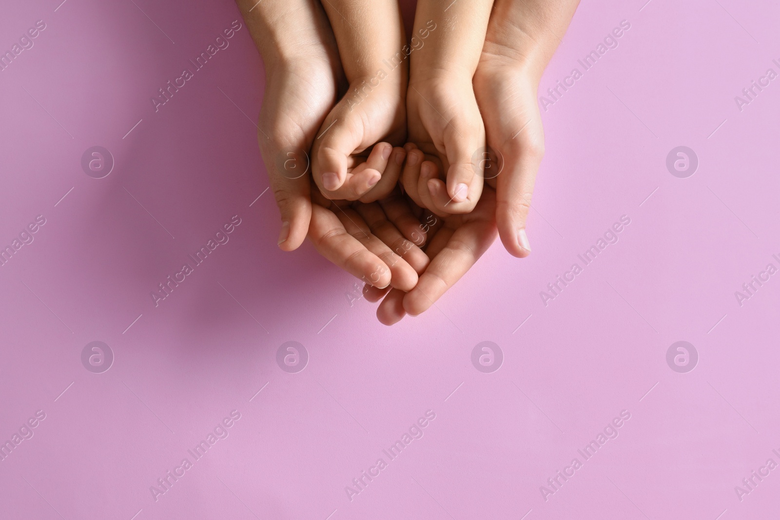 Photo of Mother holding hands with her child on pink background, top view. Happy family