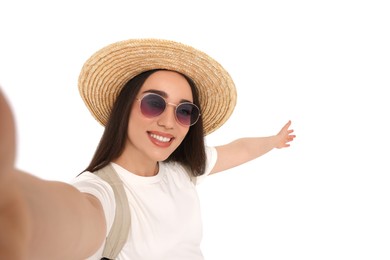 Smiling young woman in sunglasses and straw hat taking selfie on white background