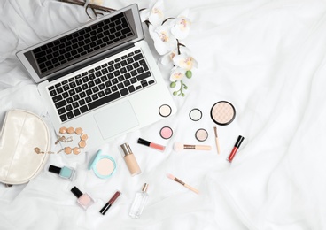 Flat lay composition with laptop and makeup products for woman on bed