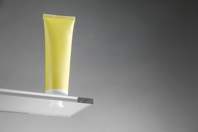 Tube with moisturizing cream on glass against grey background, low angle view. Space for text