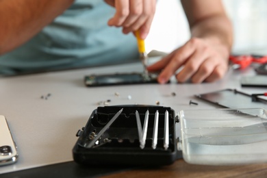 Toolbox in focus and blurred technician repairing mobile phone at table, closeup with space for text