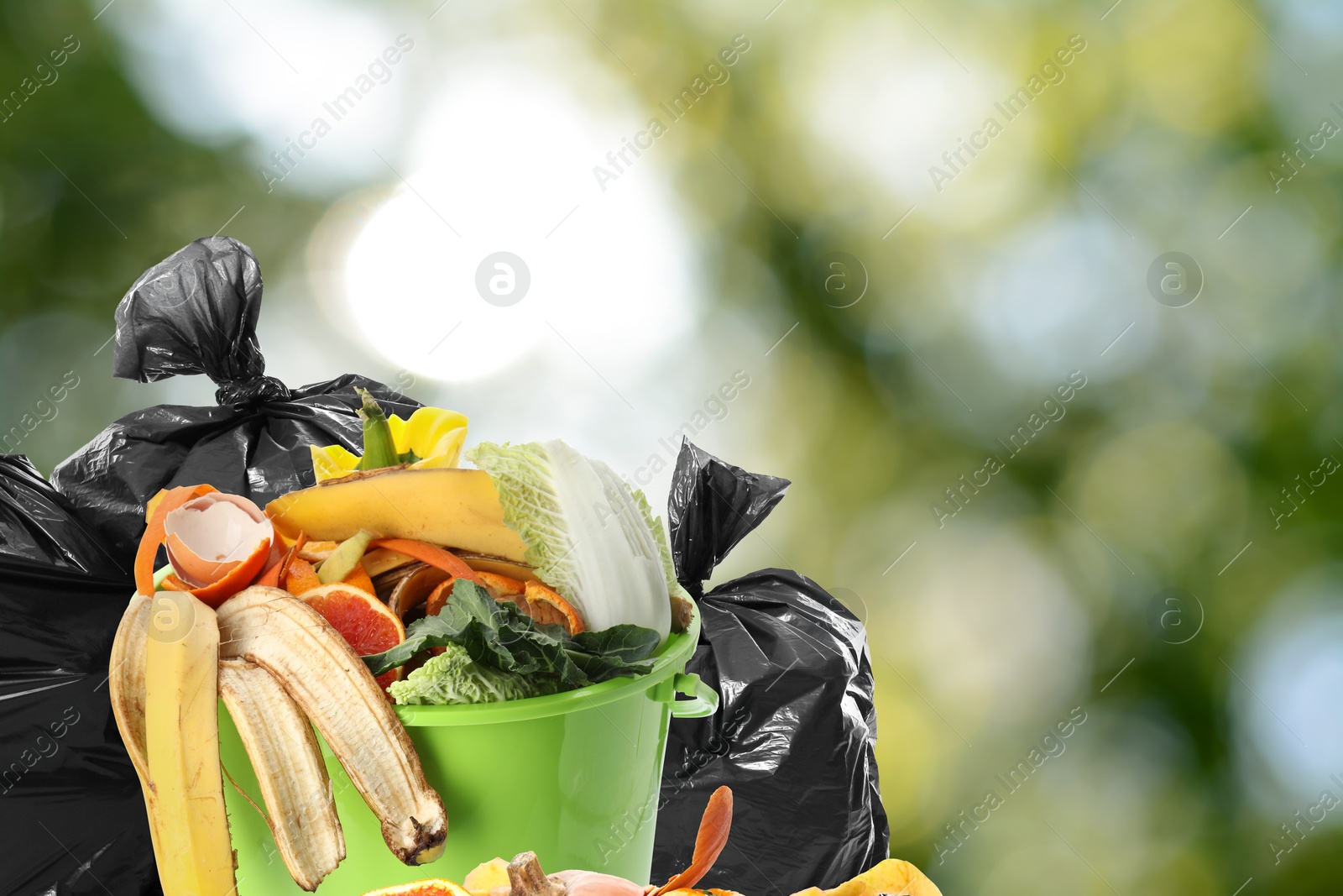 Image of Waste bin and plastic bags full of garbage on blurred background, space for text