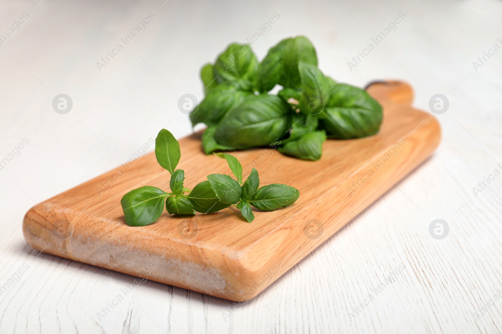 Photo of Wooden board with fresh green basil leaves on table