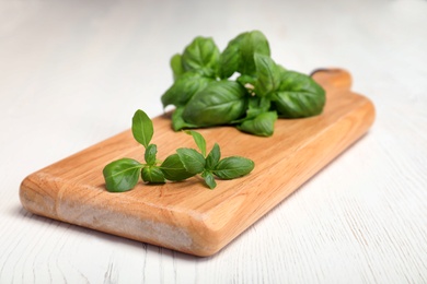 Wooden board with fresh green basil leaves on table