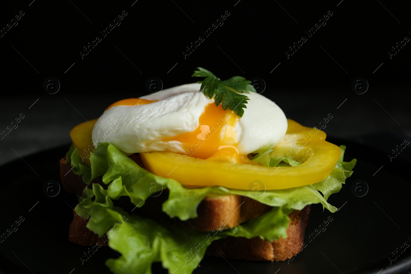 Photo of Delicious poached egg sandwich served on black plate, closeup