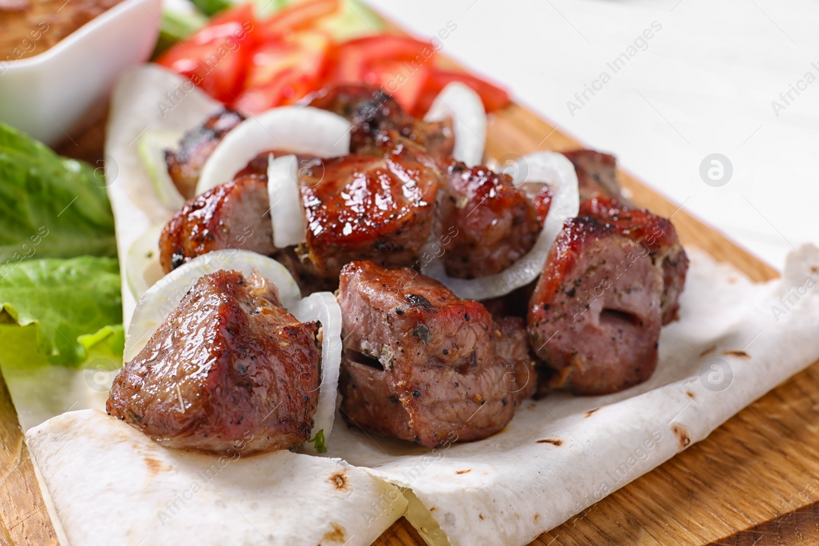 Photo of Wooden board with juicy shish kebab, closeup