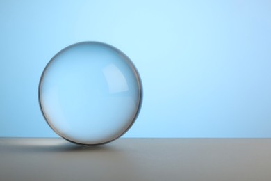 Photo of Transparent glass ball on table against light blue background. Space for text