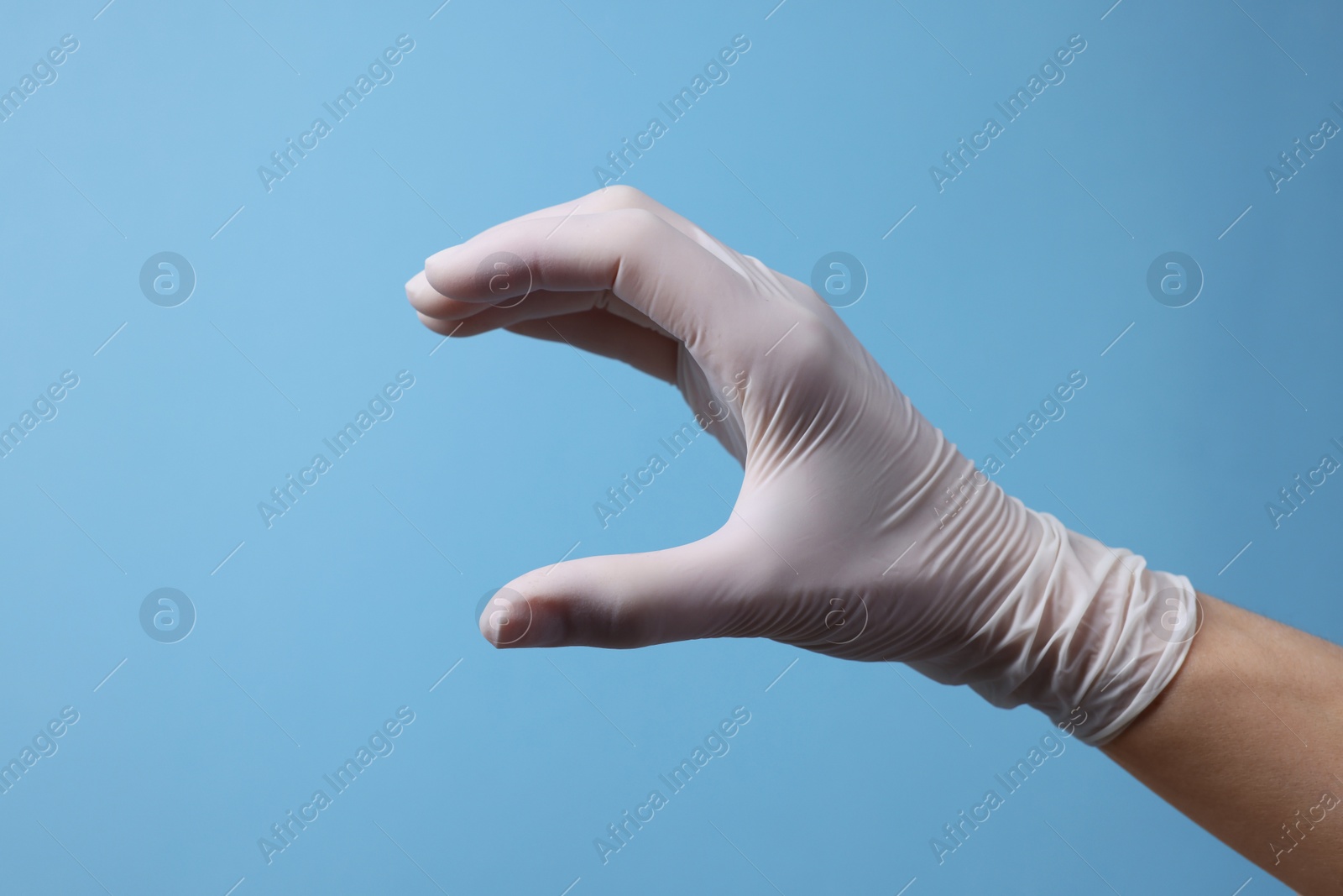 Photo of Doctor wearing white medical glove holding something on light blue background, closeup