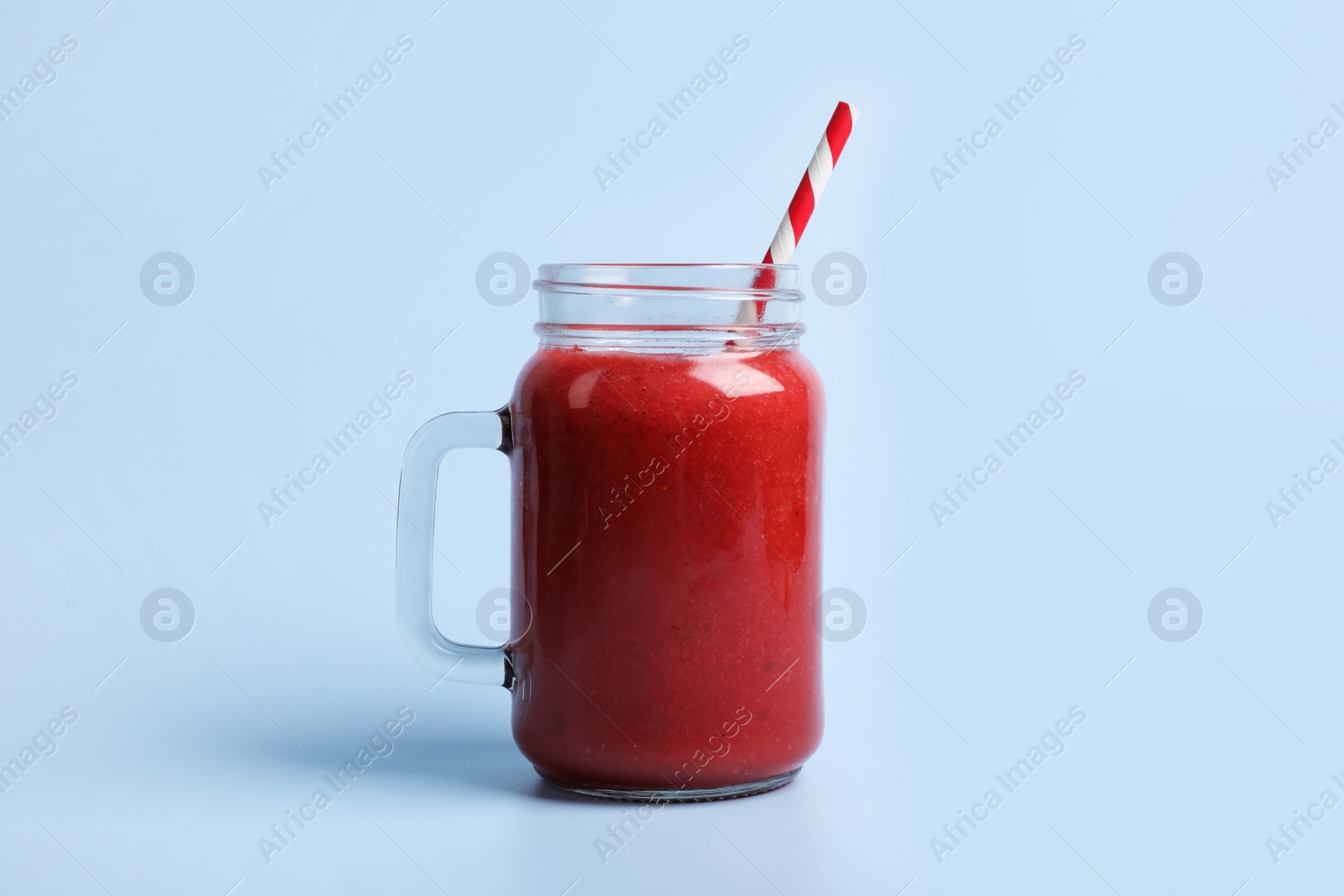 Photo of Mason jar with delicious berry smoothie on light blue background