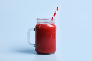 Mason jar with delicious berry smoothie on light blue background